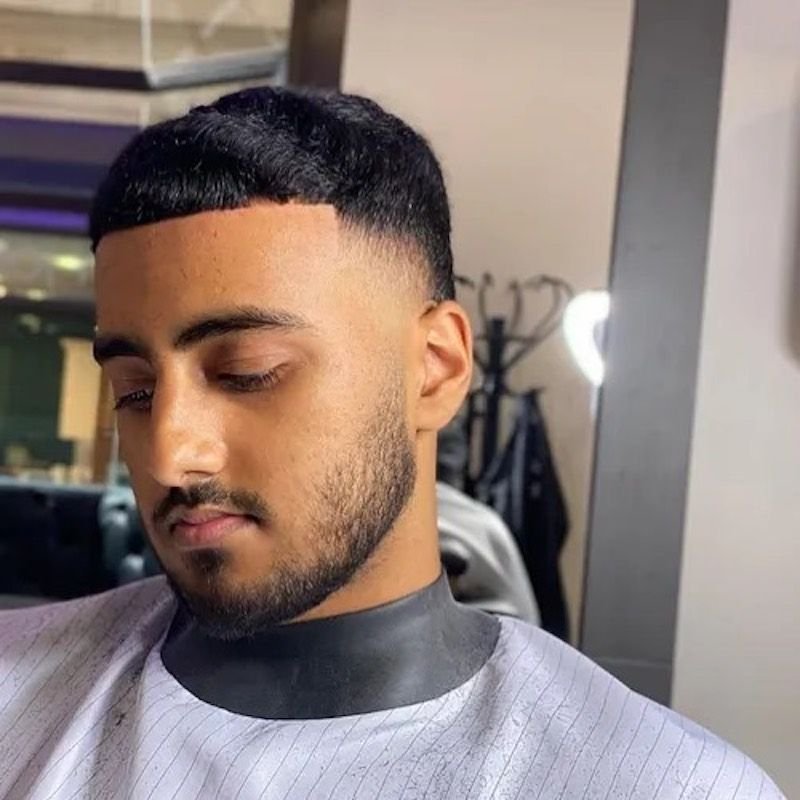 رجل بتسريحة "قصة الوعاء" (Bowl cut) القصيرة، مع جوانب متدرجة ولحية قصيرة