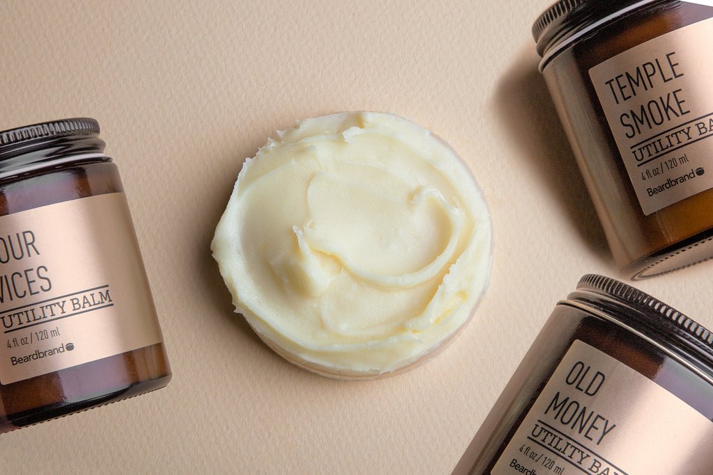 كمية دائرية من بلسم "Beardbrand Utility Balm" موضوعة على طاولة، ومحاطة بثلاث عبوات من نفس المنتج.
